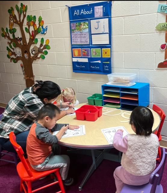 Adult and three children sitting at a table, coloring
