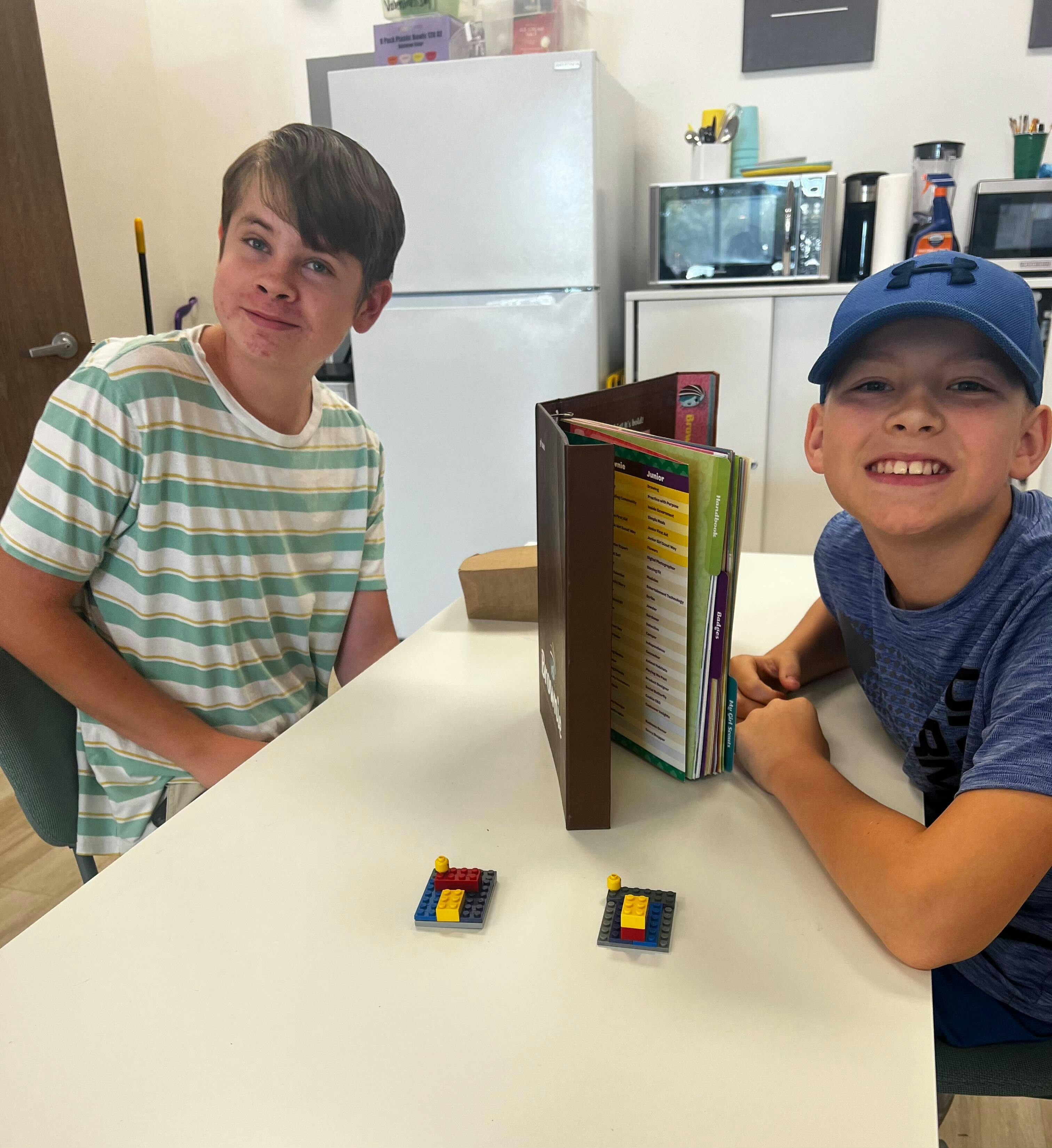 Two children sitting at a table with a book and small objects