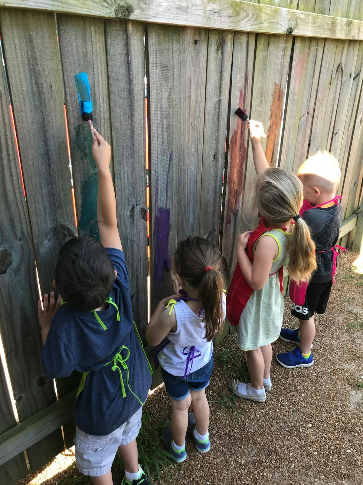 Four children painting on a wooden fence