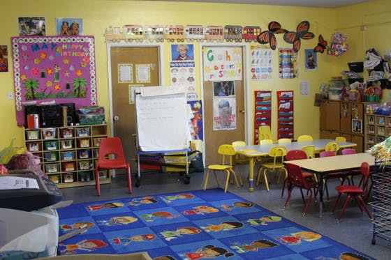 Classroom with a blue rug, small tables and chairs, and a whiteboard