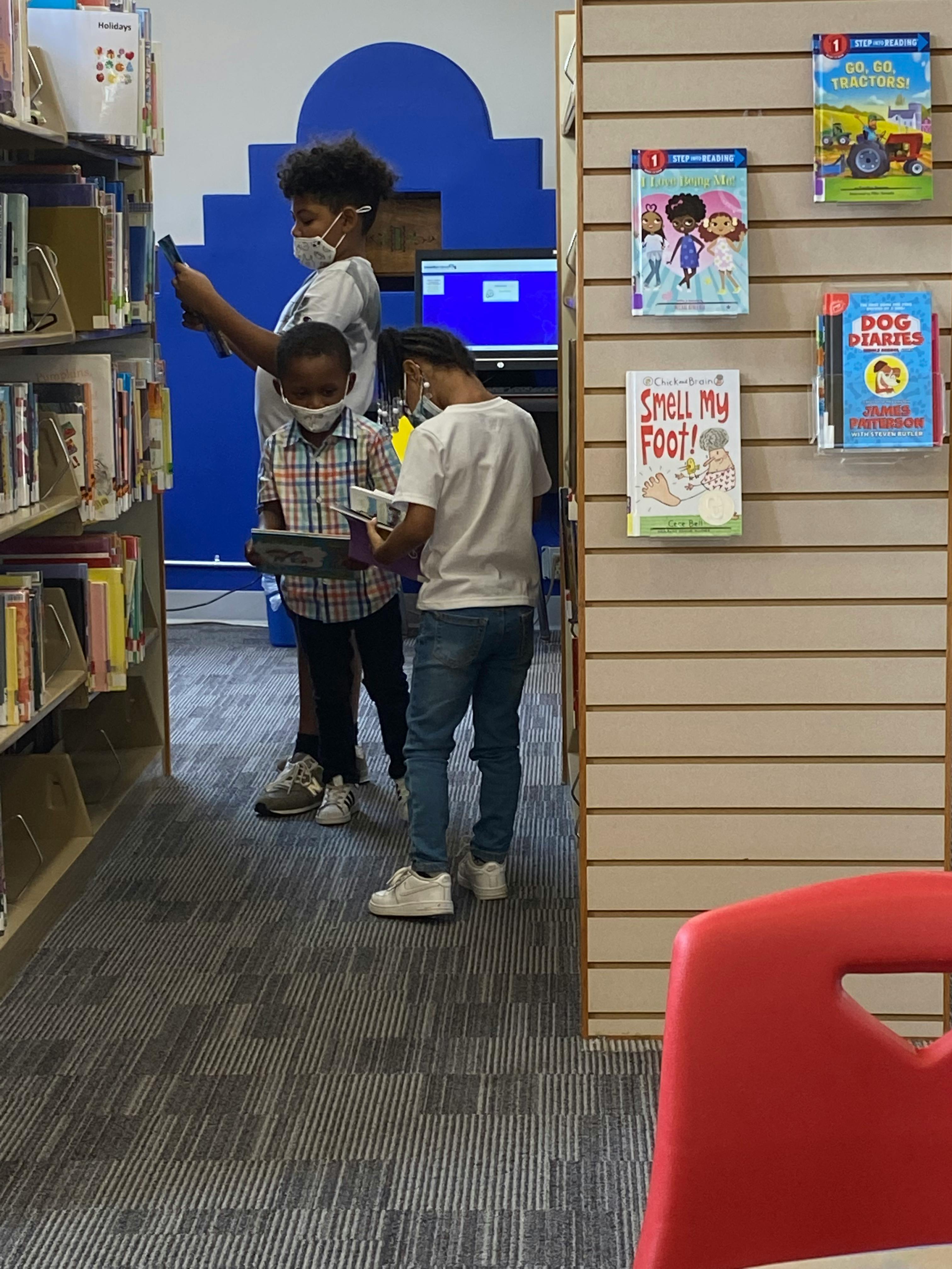 Three children in masks looking at books in a library