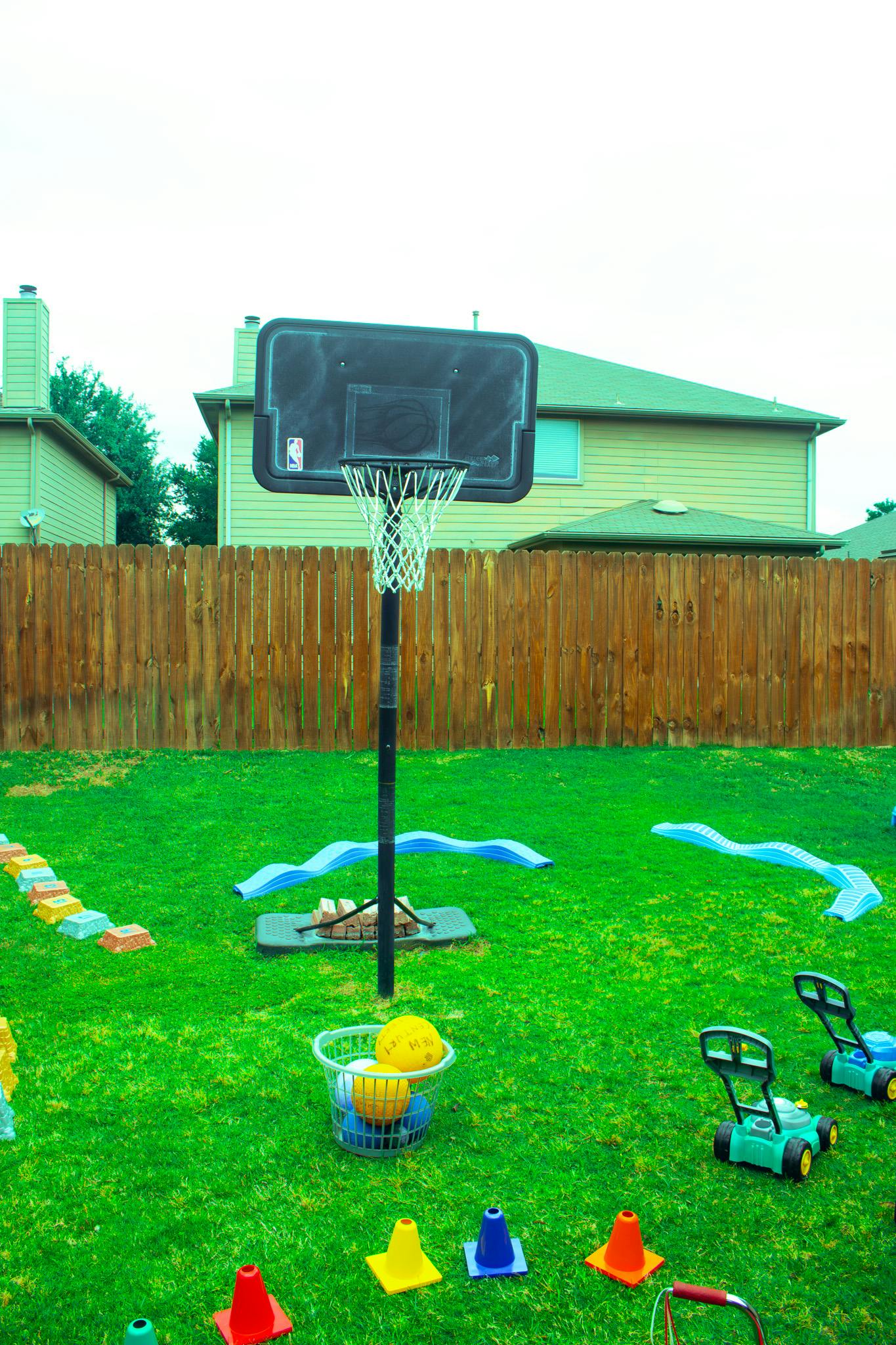Basketball hoop on a green lawn with colorful toys and a wooden fence