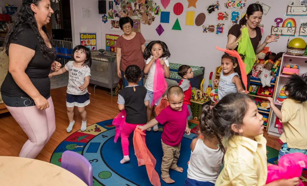 Adults and children in a classroom, some holding colorful fabrics