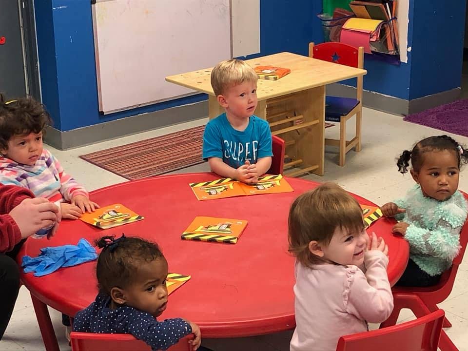Five children sitting around a red table in a classroom