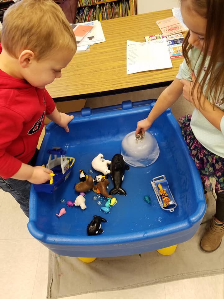 Two children playing with animal toys in a blue water table