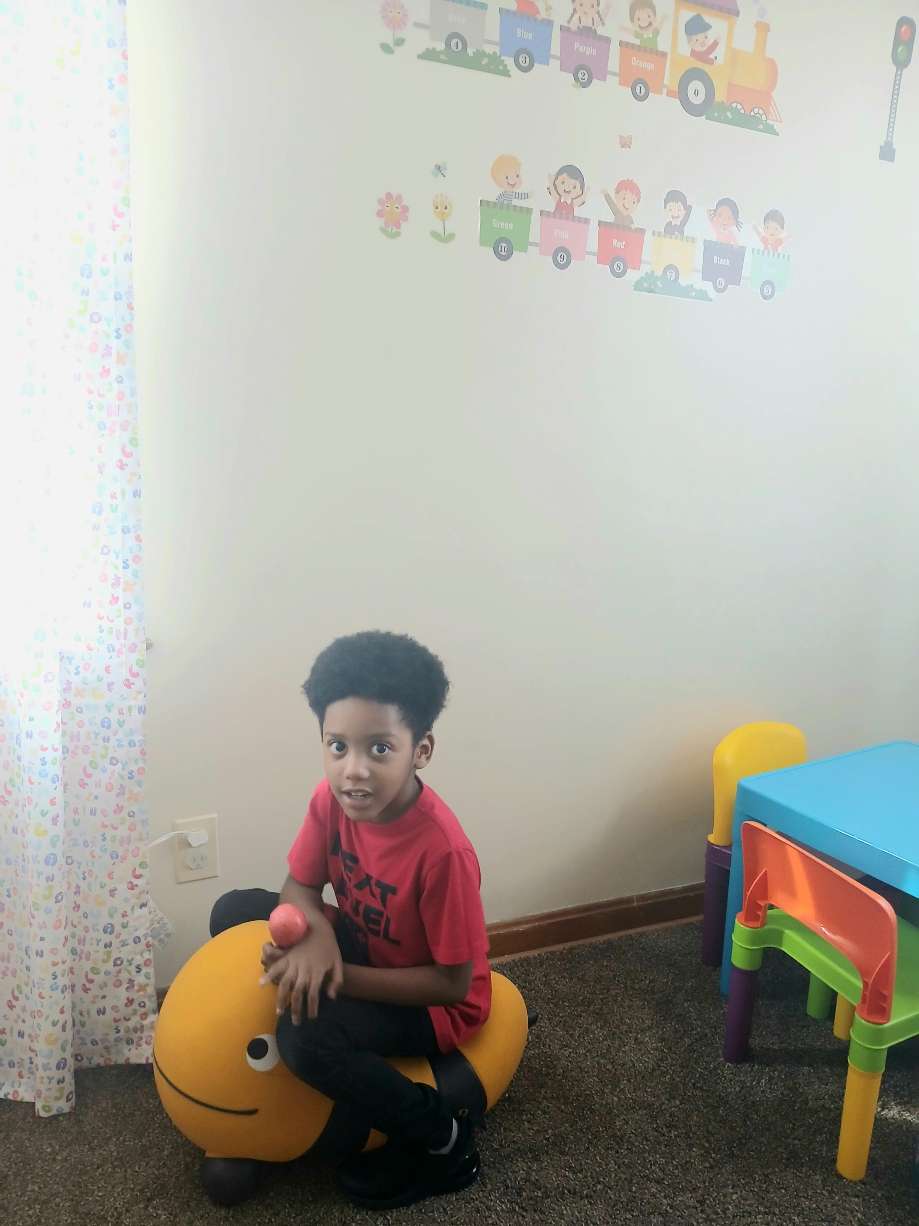 Child sitting on a yellow toy in a room