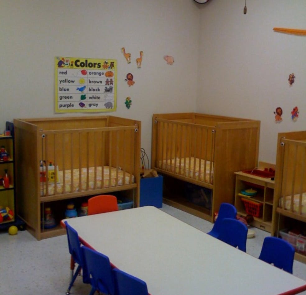 Nursery room with multiple wooden cribs and a table with blue chairs
