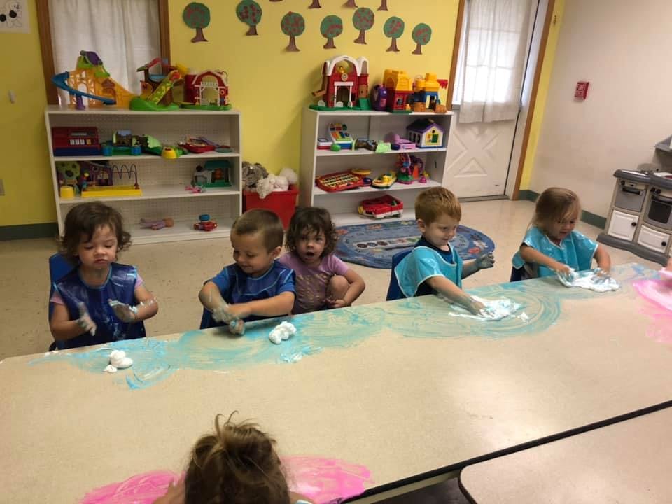 Children sitting at a table doing an art activity with paint
