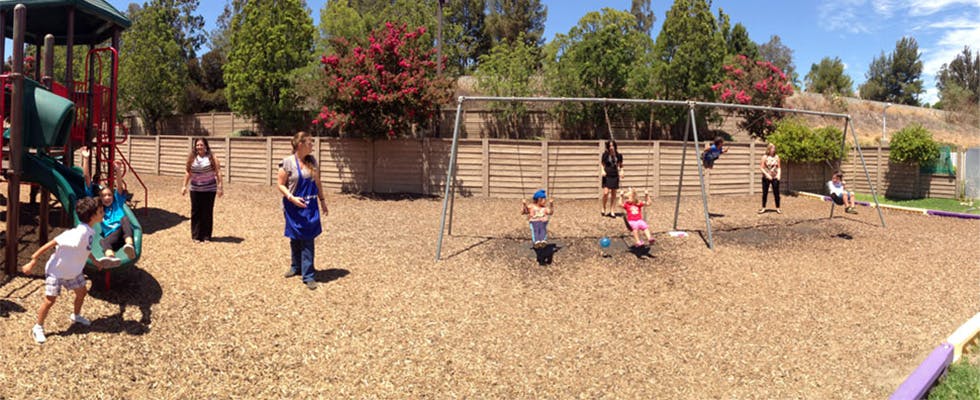 People and children on a playground with swings and play structure