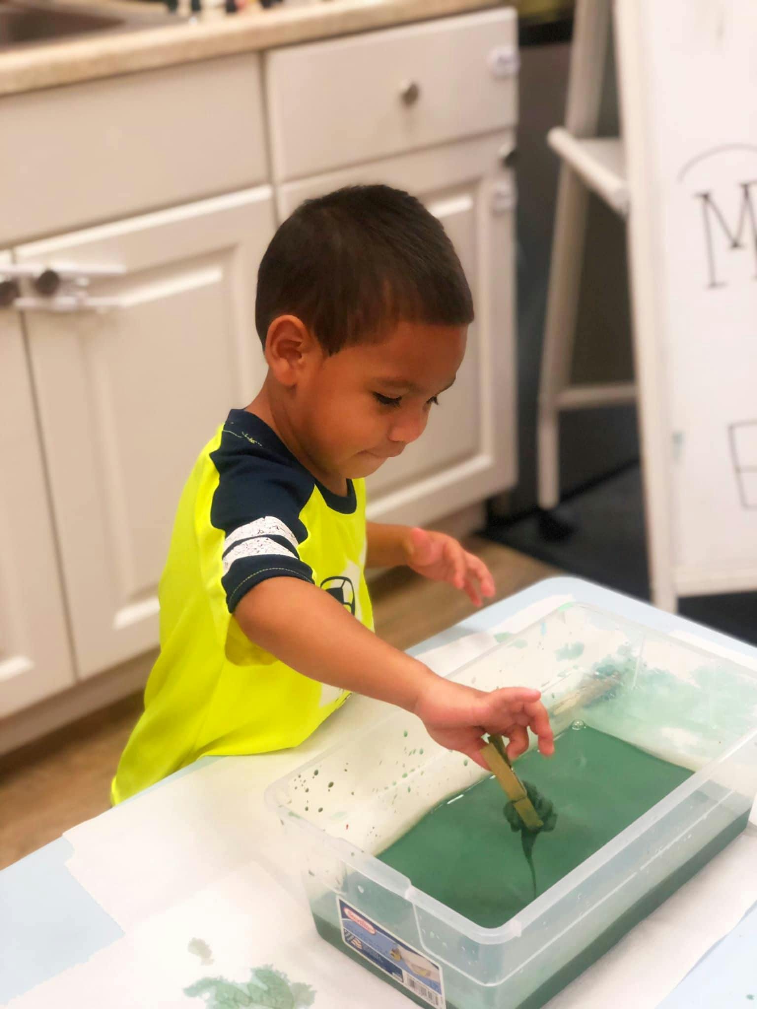 Child painting with green paint in a container
