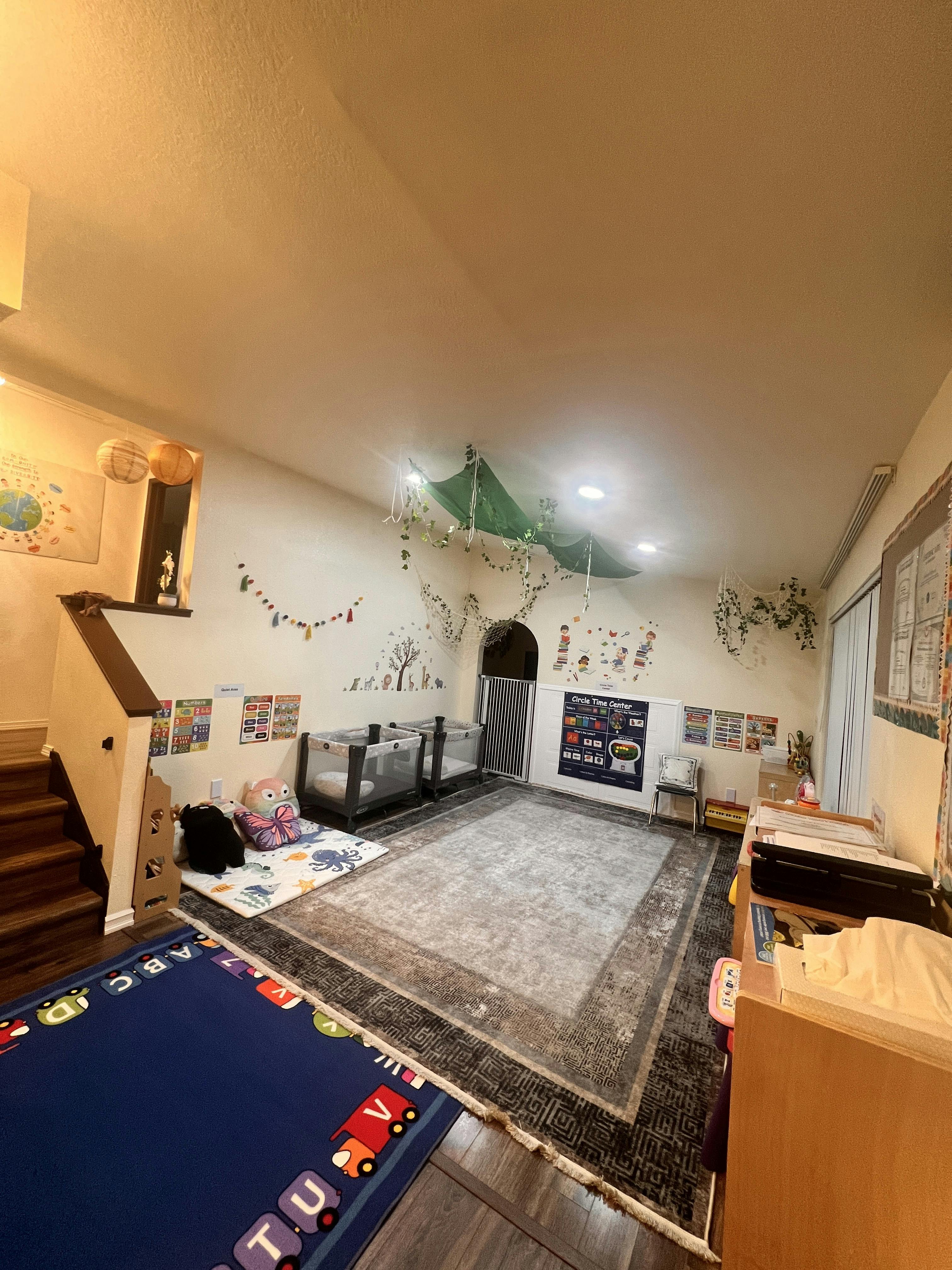 Childcare room with play mats, pack and plays, and educational wall charts