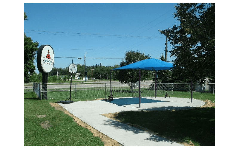 Sign for KinderCare next to a basketball hoop and a blue shade structure with a canopy