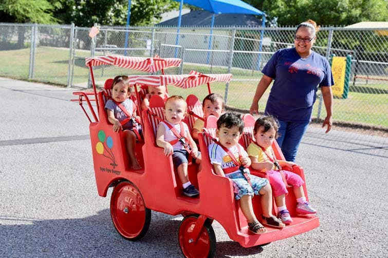 Person pushing a red multi-seat stroller with several children