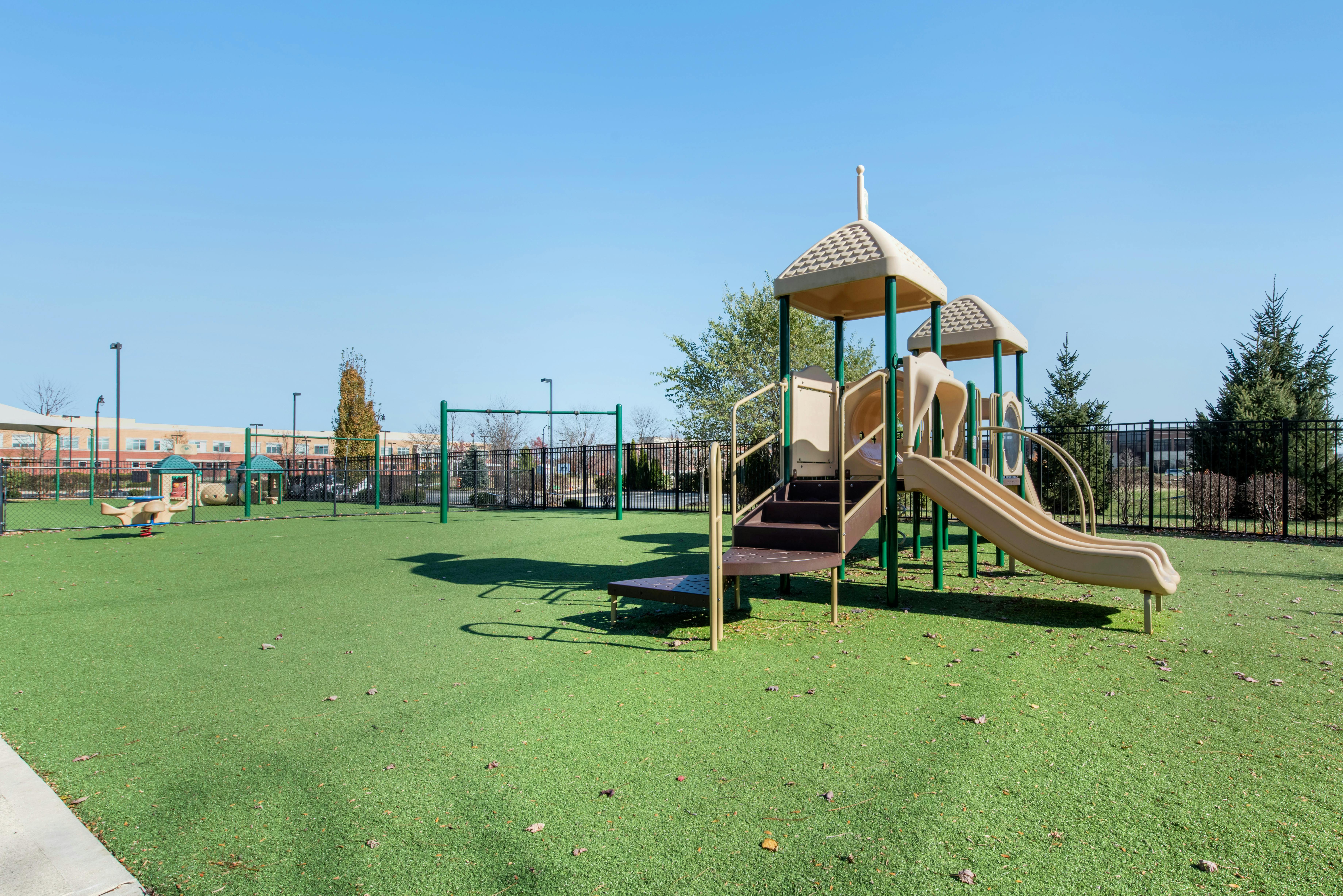 A playground with a slide, climbing structure, swings, and a spring rider on artificial turf