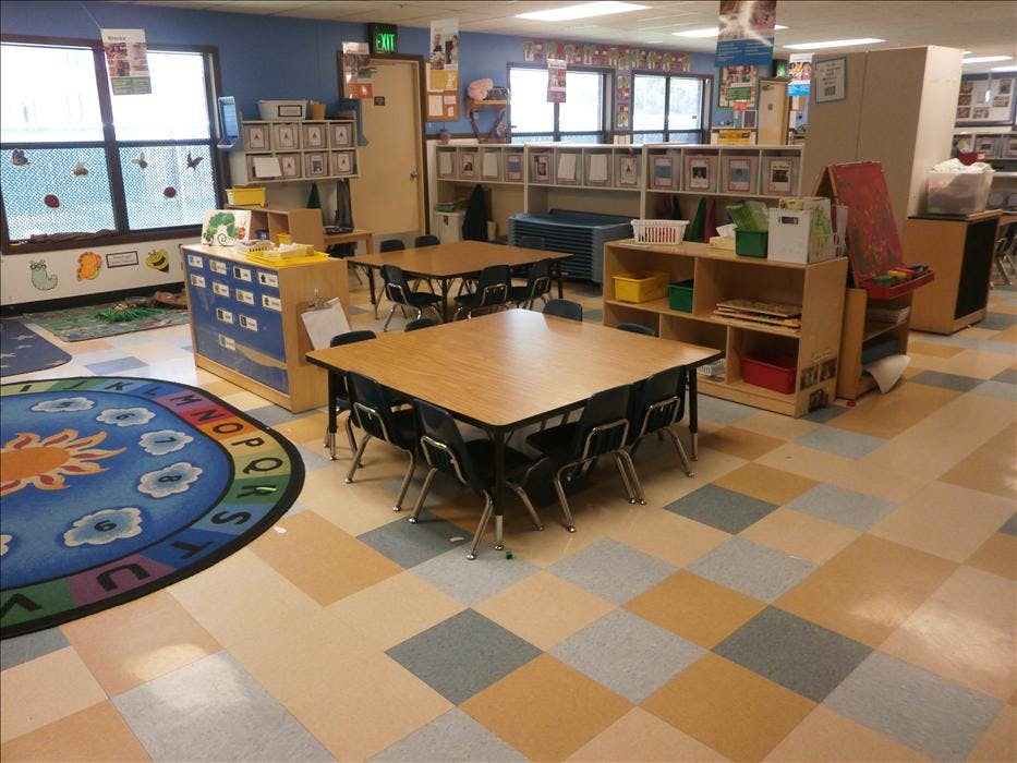 Classroom with small tables and chairs, shelves, and a circular rug