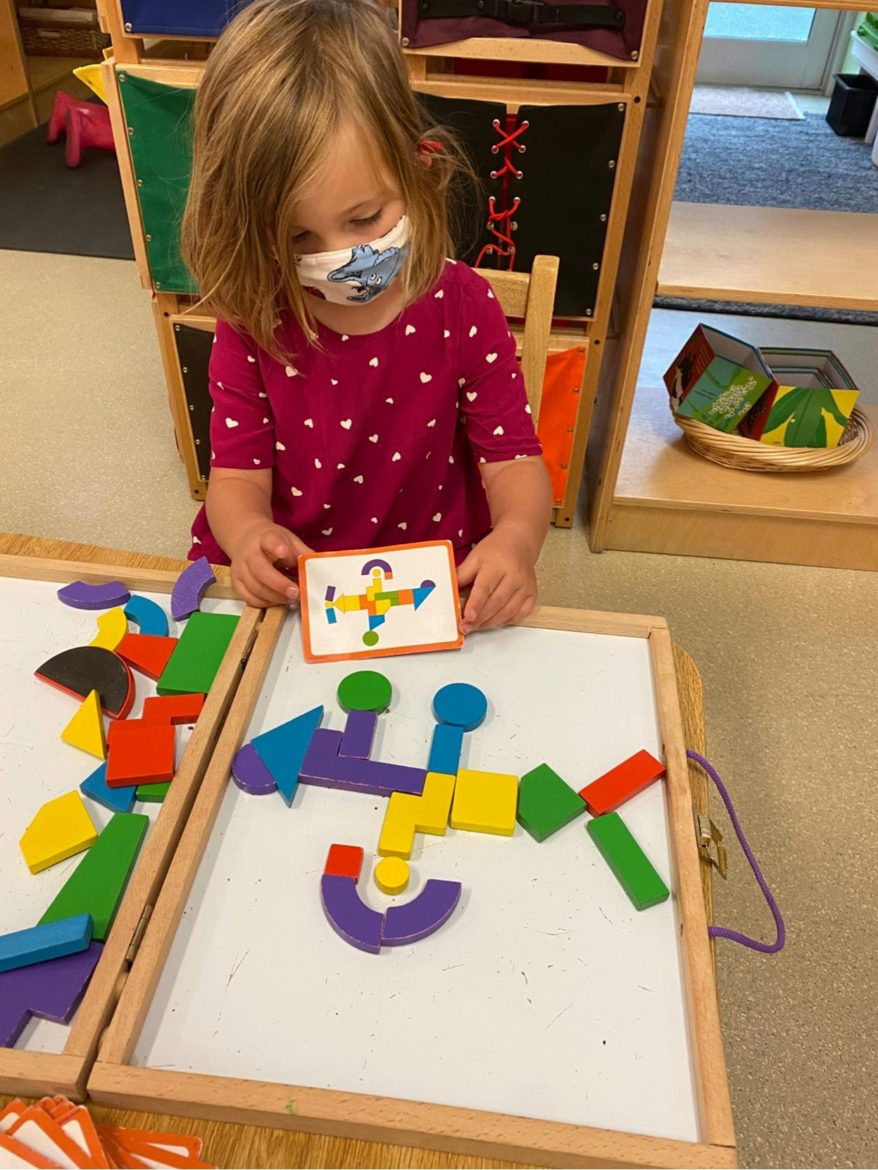 Child in a mask holding a card with a shape puzzle design