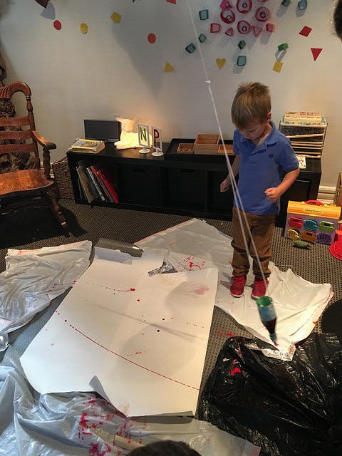 Child playing with a string and a bottle over paper on the floor