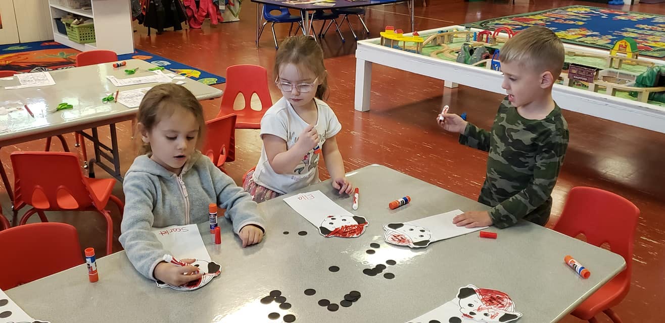 Three children doing crafts at a table in a classroom