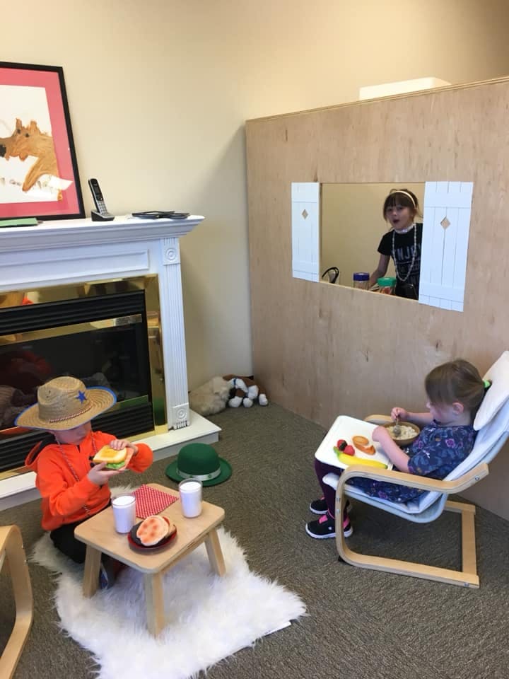 Three children playing in a room, one holding a toy sandwich