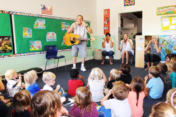 Adults playing guitar and singing to children in a classroom