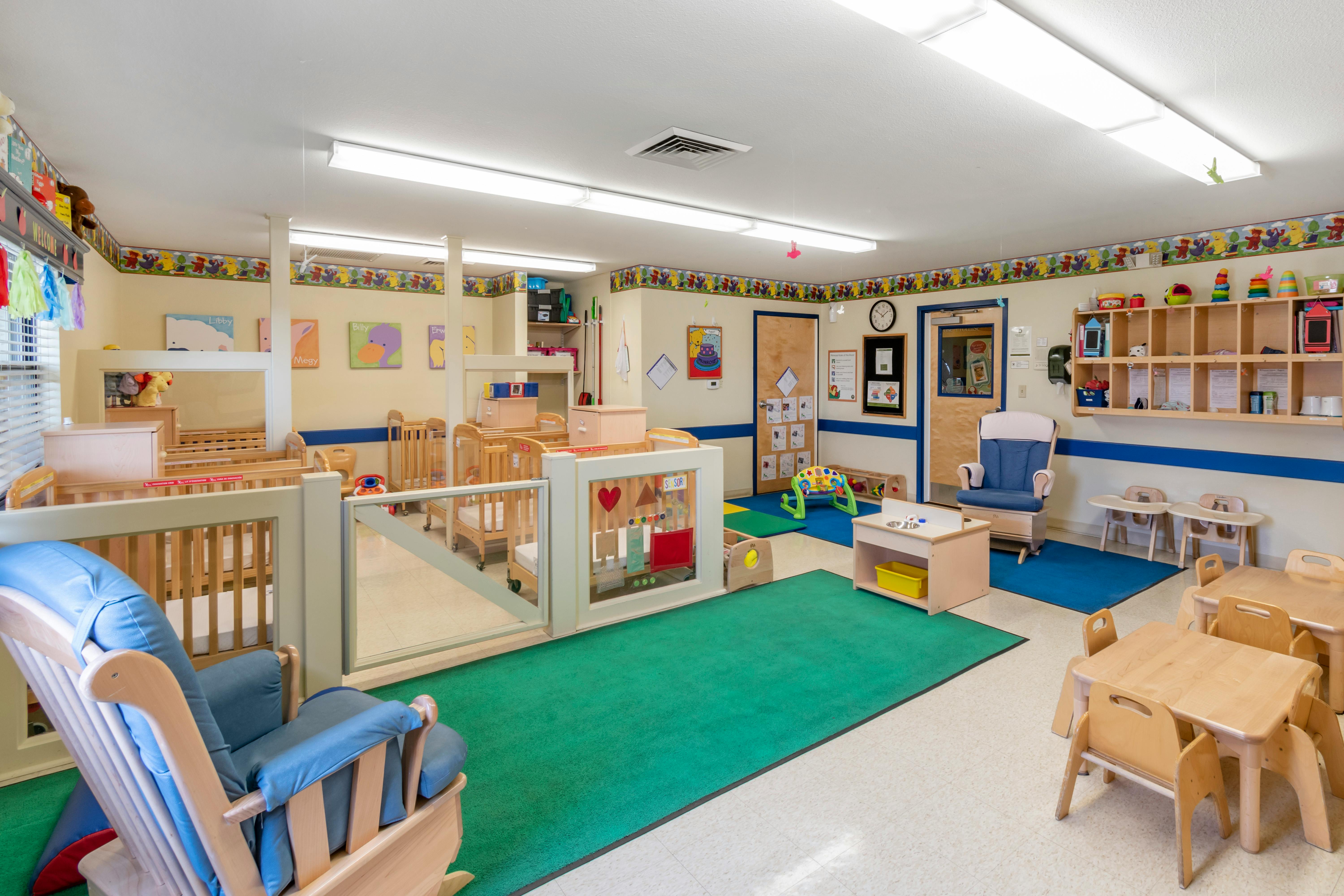 A colorful childcare room with cribs, play areas, and small tables with chairs