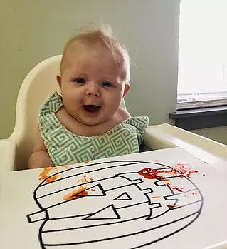 Child in high chair with a pumpkin drawing and red smudges on the tray