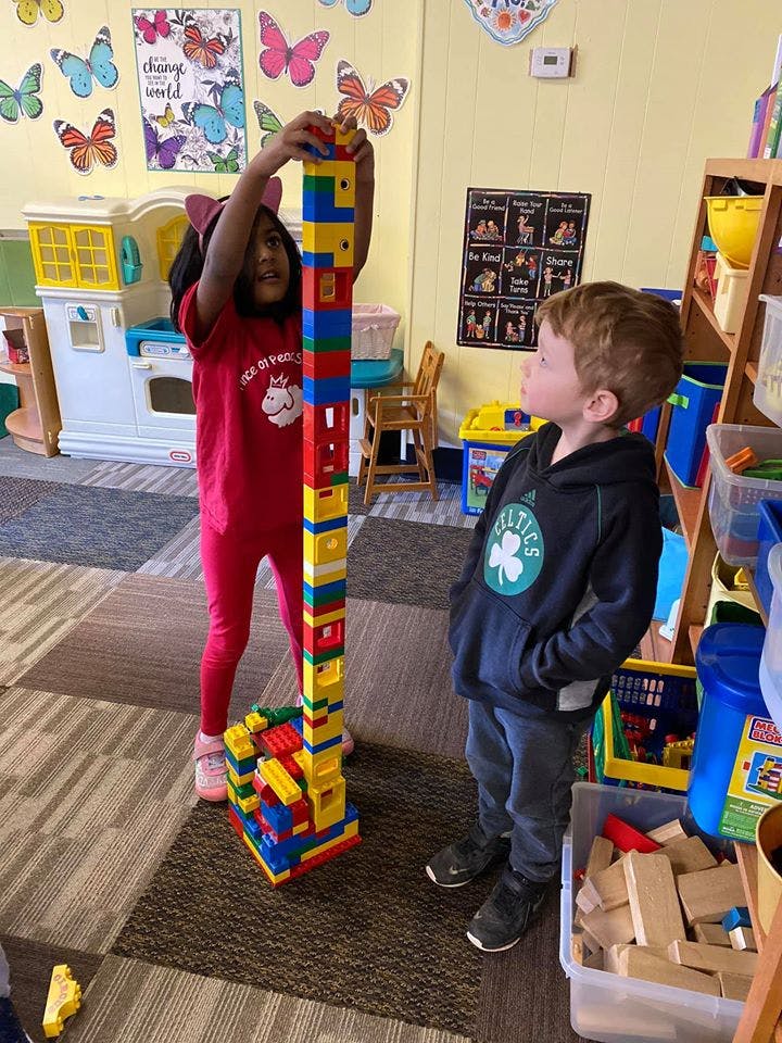 Child building a tall block tower while another child watches