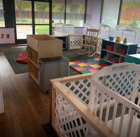 Nursery room with multiple cribs, a rocking chair, and colorful play mat
