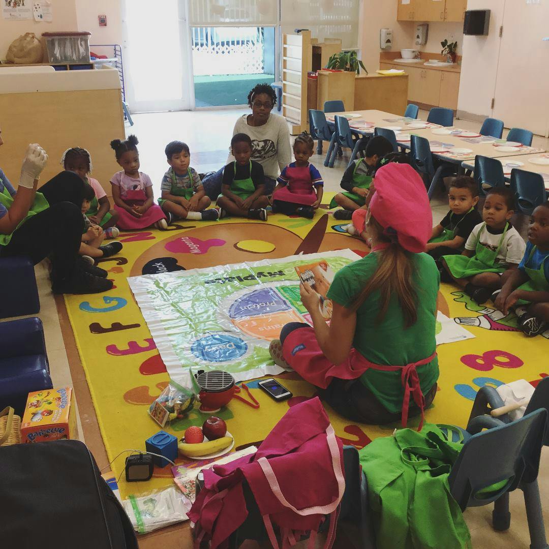 Person teaching children sitting on a colorful rug in a classroom