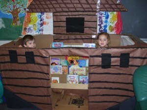 Two children playing in a cardboard playhouse