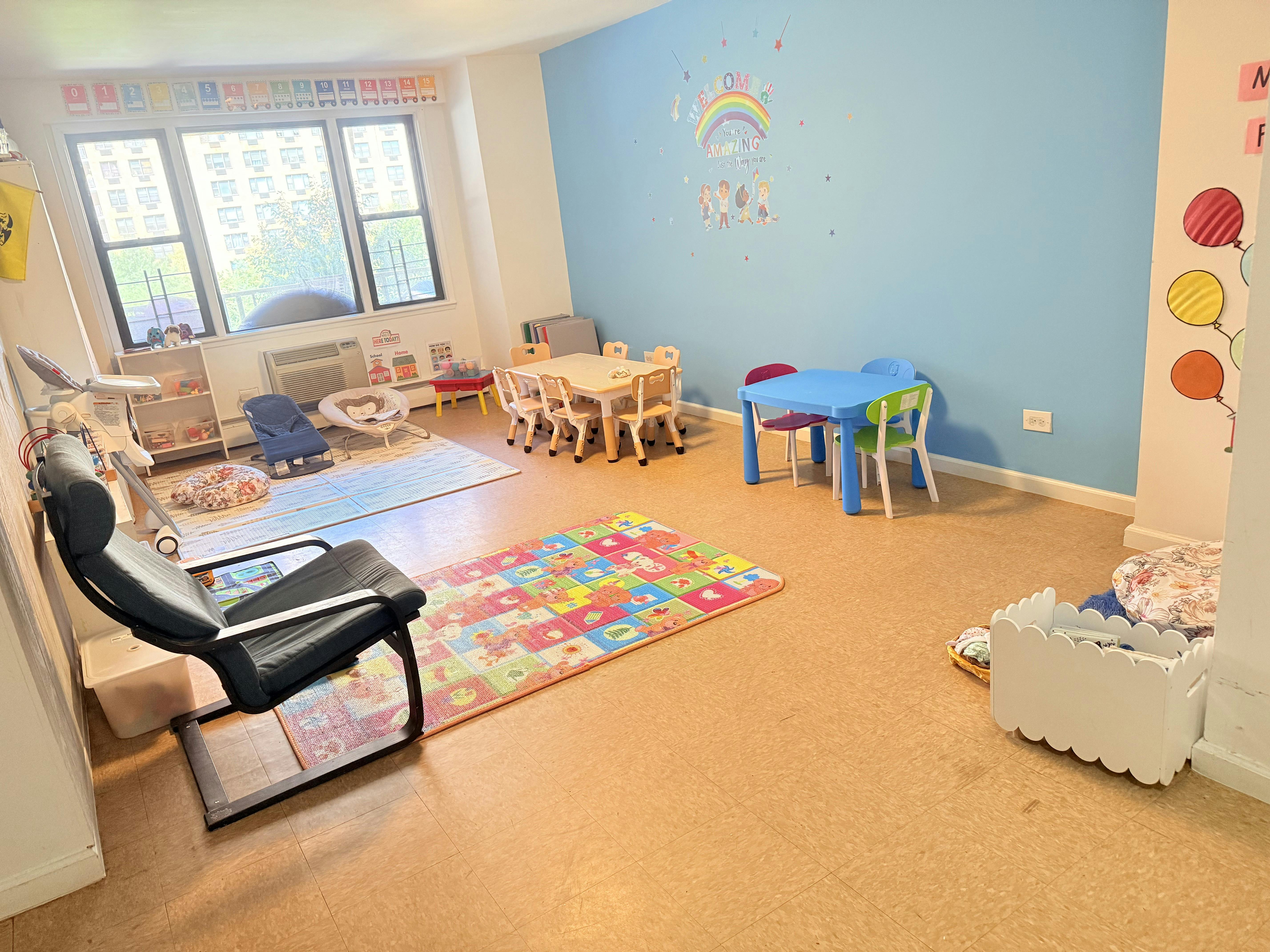 Classroom with small tables and chairs, colorful rugs, and a window