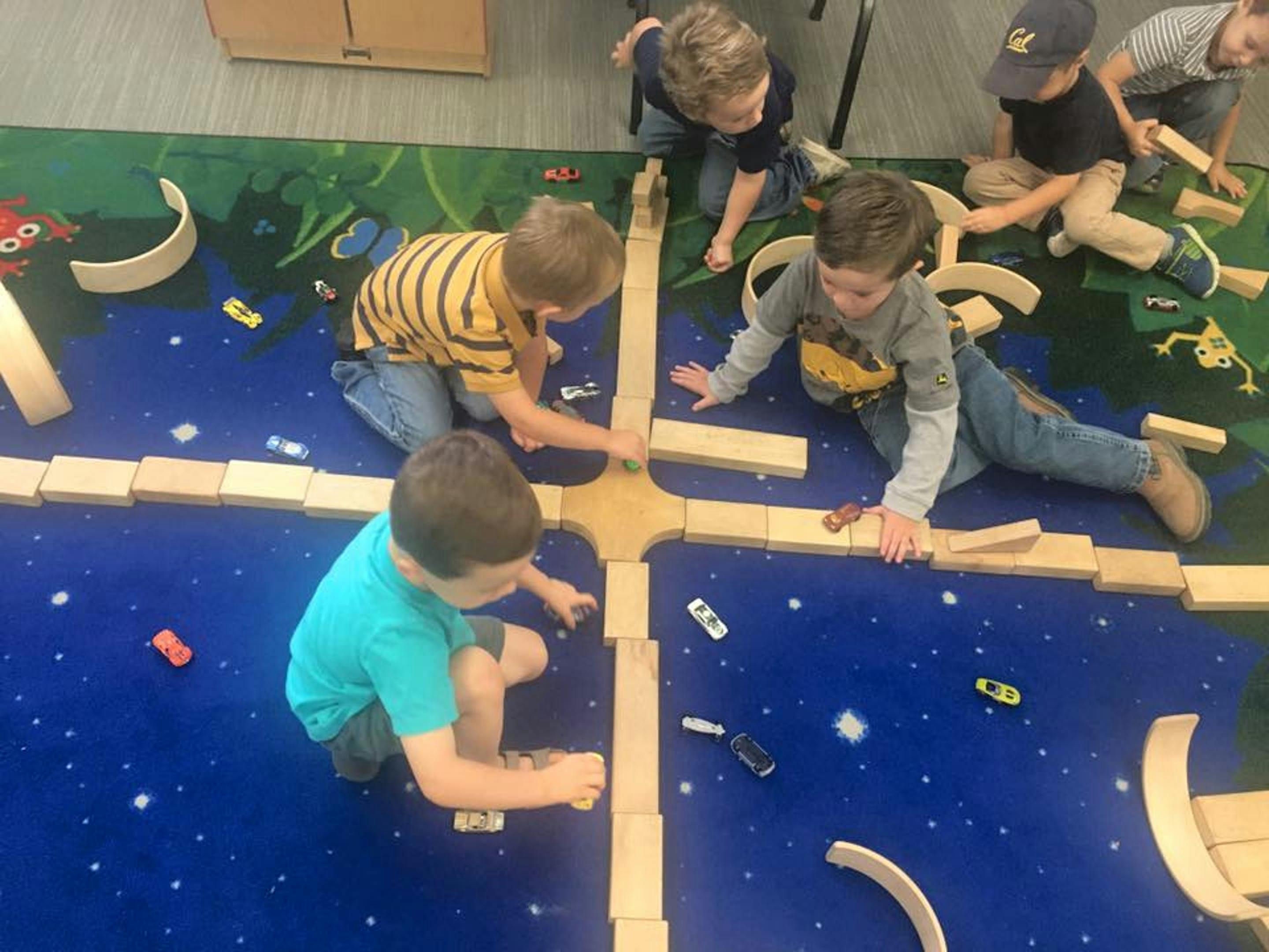 Children playing with wooden blocks and toy cars on a blue mat