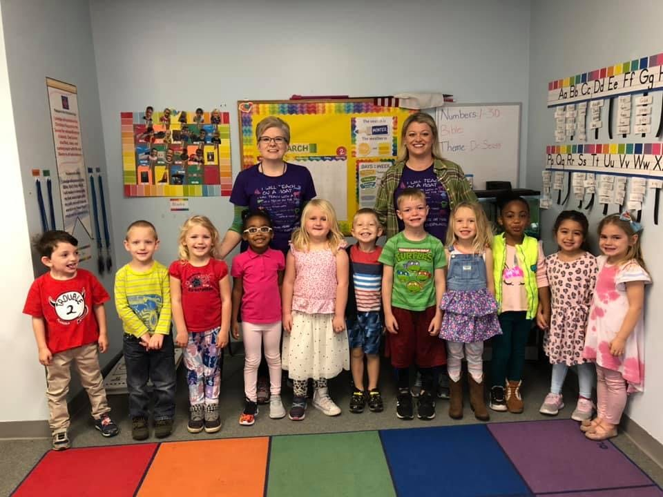 Two adults and a group of children standing in a classroom