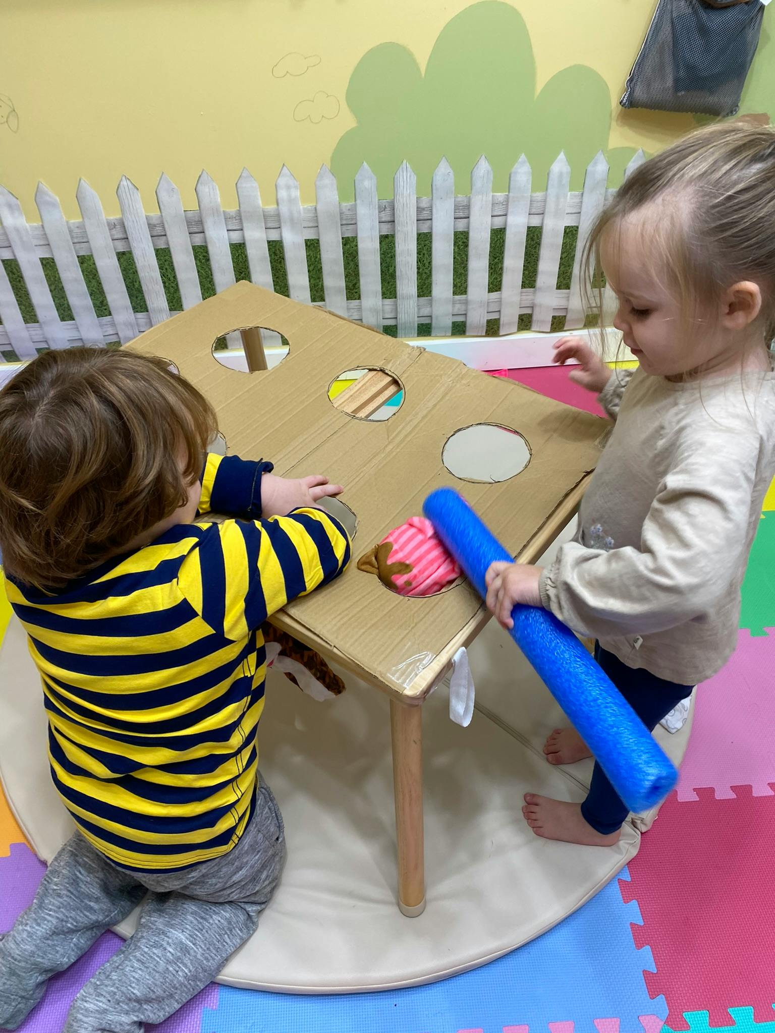 Two children playing with a cardboard box on a small table