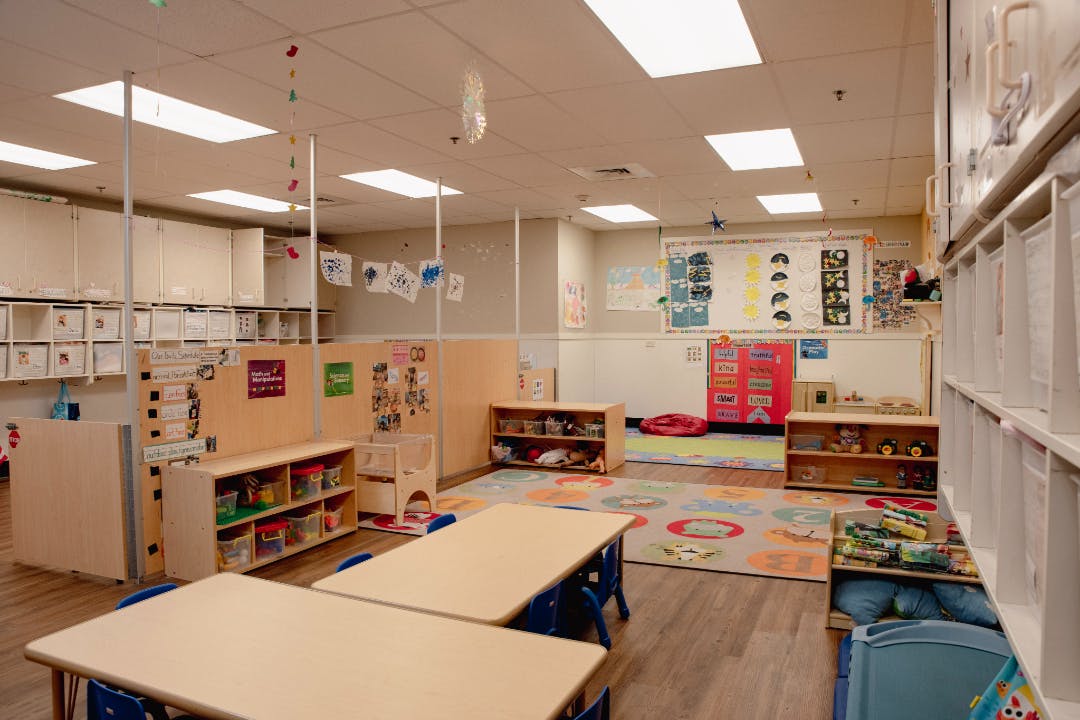 Empty classroom with tables, chairs, colorful rug, and cubbies