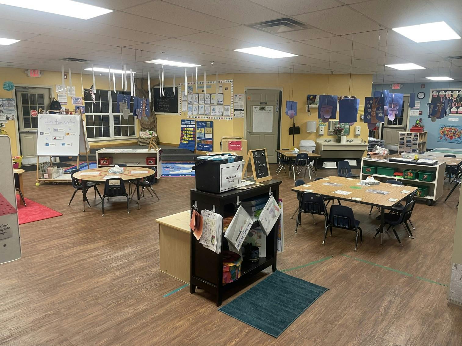 An empty classroom with several tables and chairs, whiteboards, and learning materials