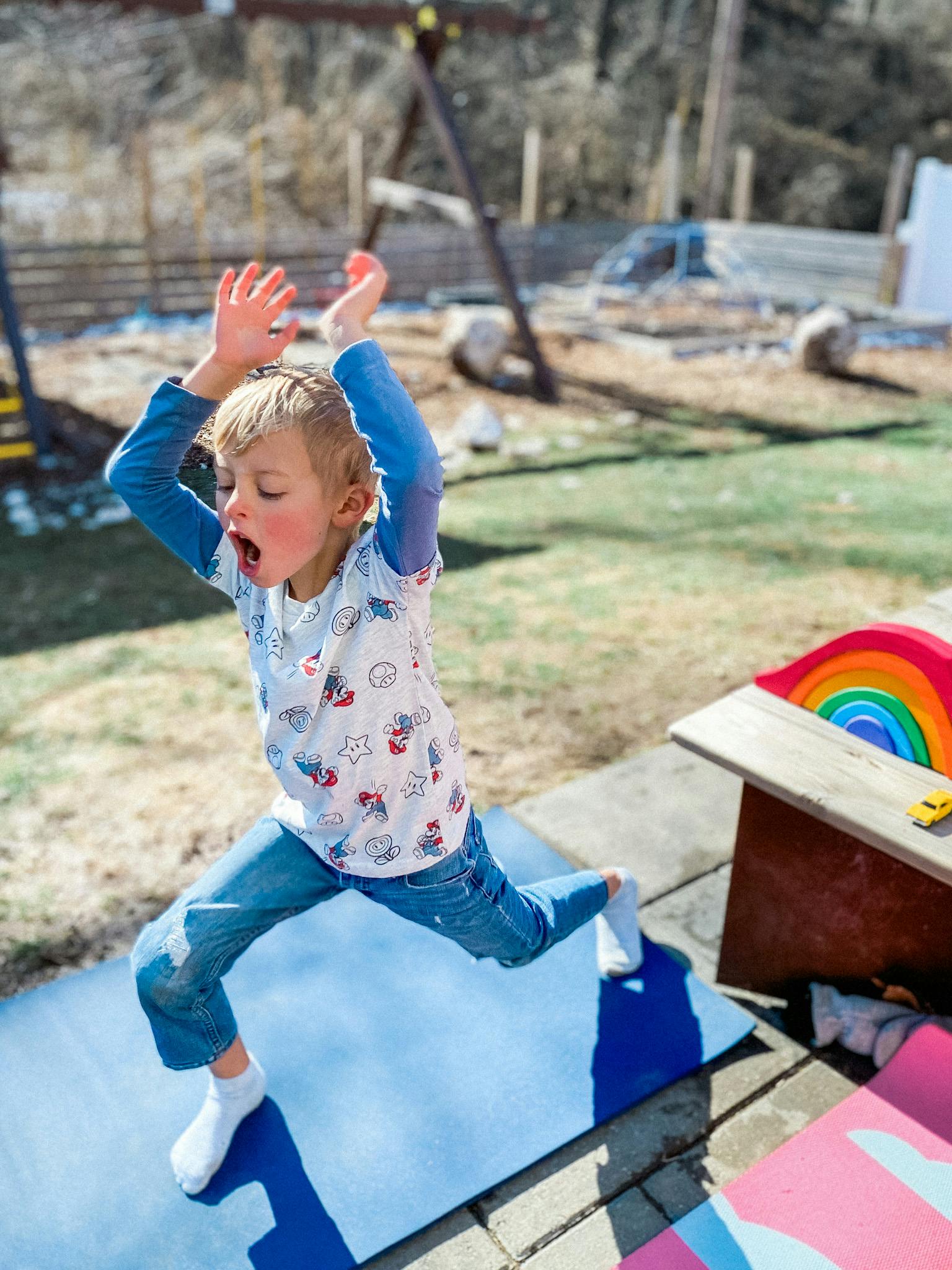 Child on a blue mat with arms raised and mouth open
