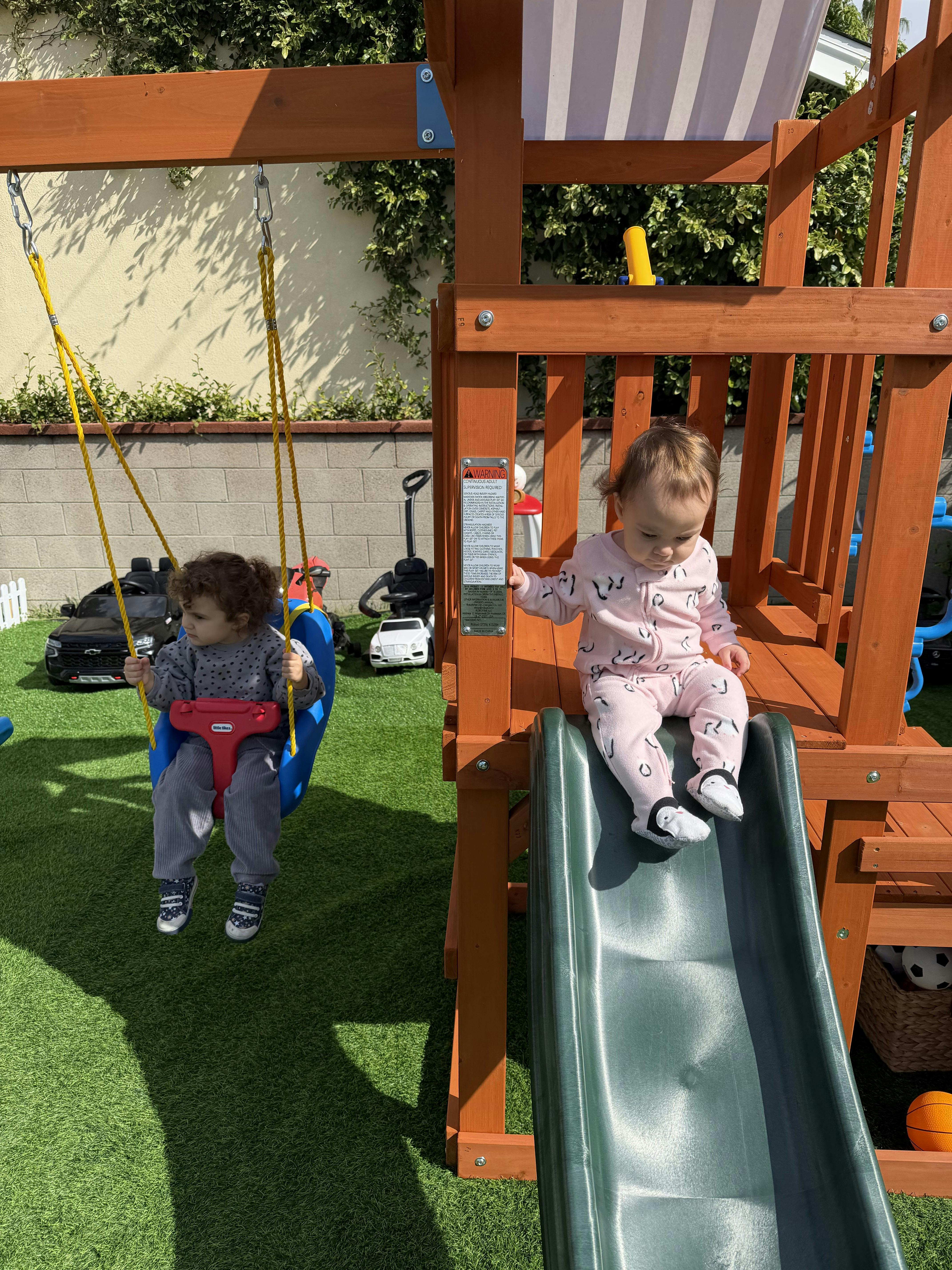Child on a swing next to a child sitting on a slide