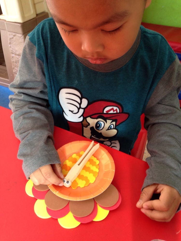 Child playing with a craft turkey on a red table