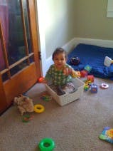 Child sitting in a plastic bin surrounded by toys
