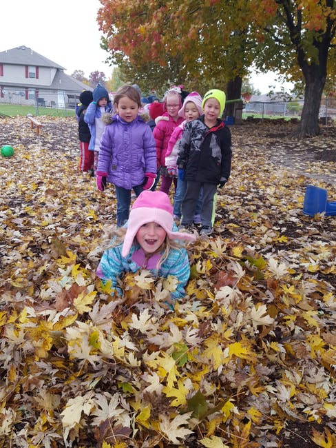 Child in a pile of leaves with other children standing behind