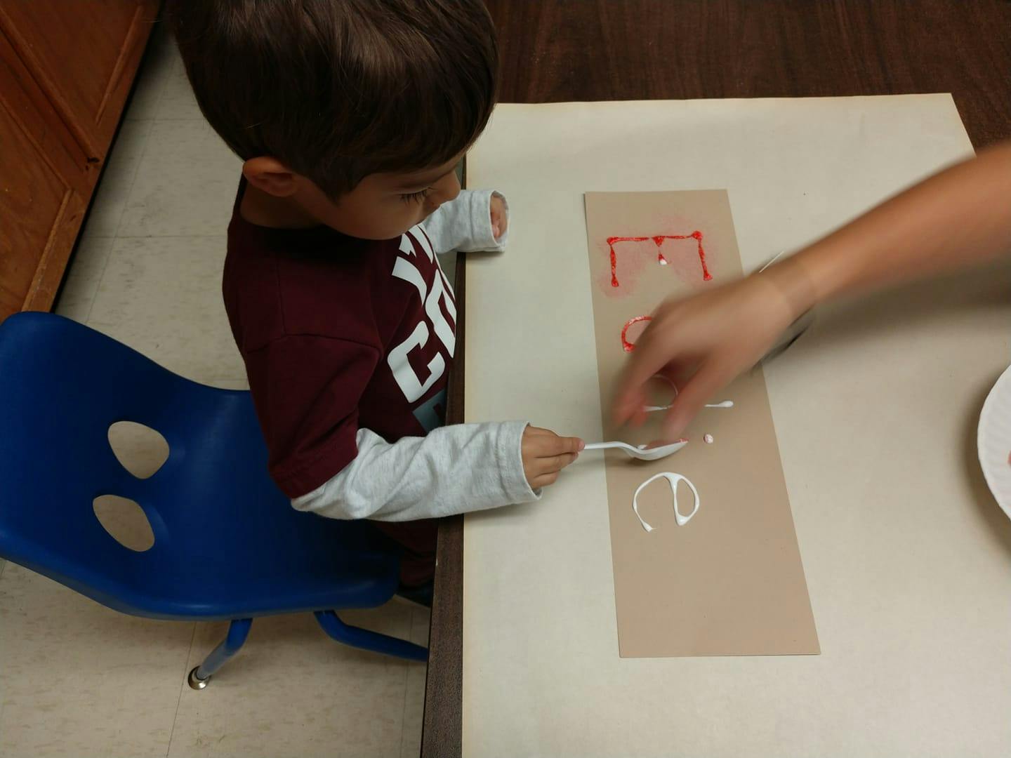 Child and adult applying glue to paper with letters