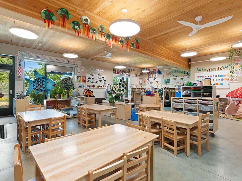 Empty classroom with small wooden tables and chairs, artwork on walls