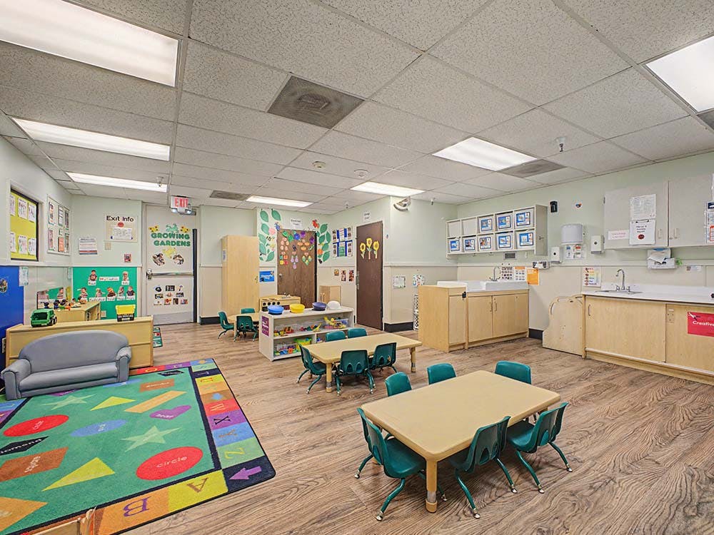 empty preschool classroom with small tables and chairs, play area