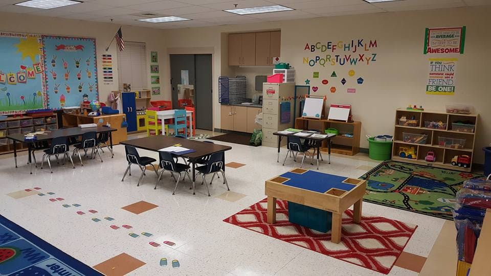 Empty classroom with small tables and chairs, alphabet on wall