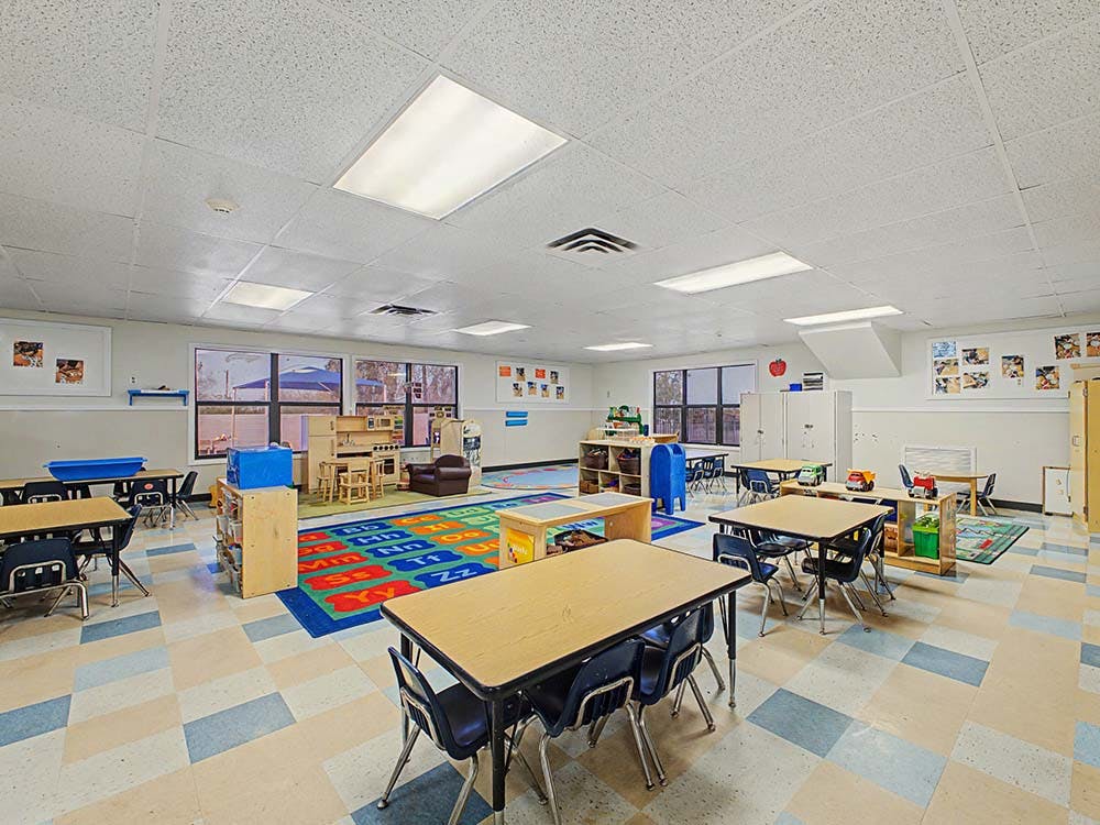 Classroom with small tables and chairs, a play kitchen, and an alphabet rug