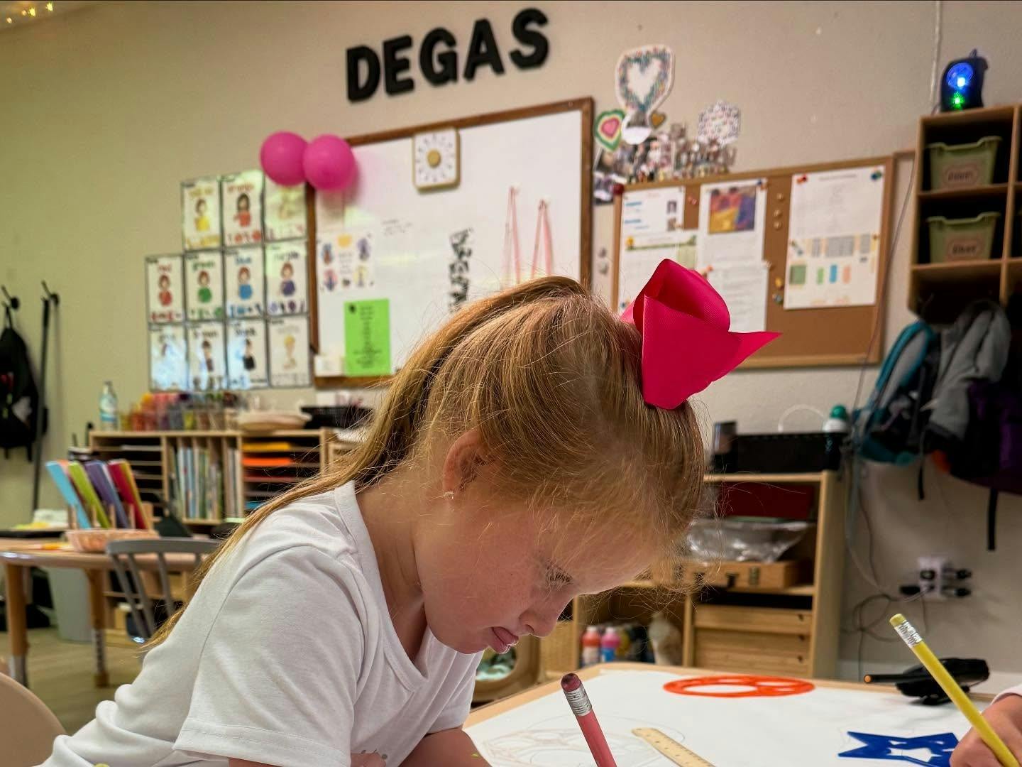 Child with a pink bow drawing in a classroom
