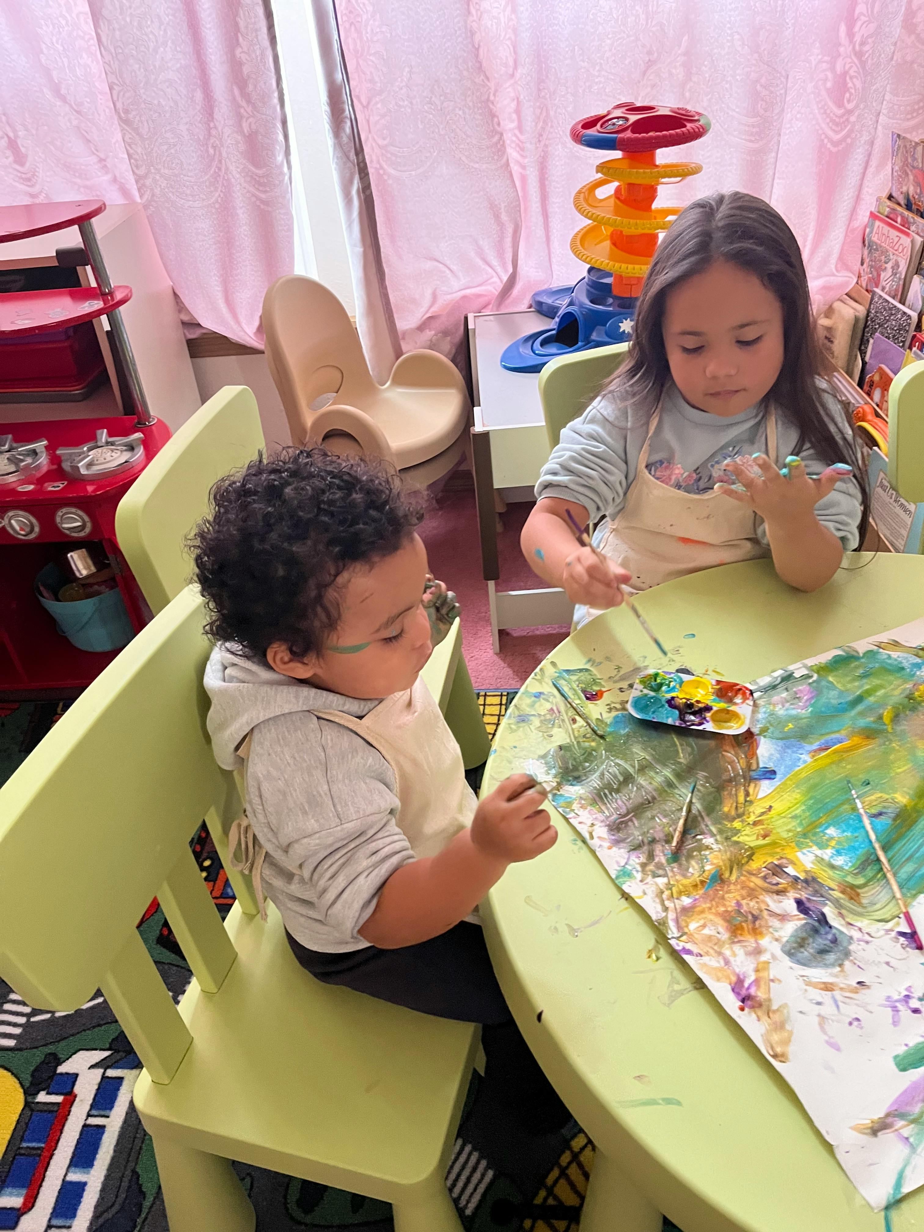 Two children painting at a table in a classroom