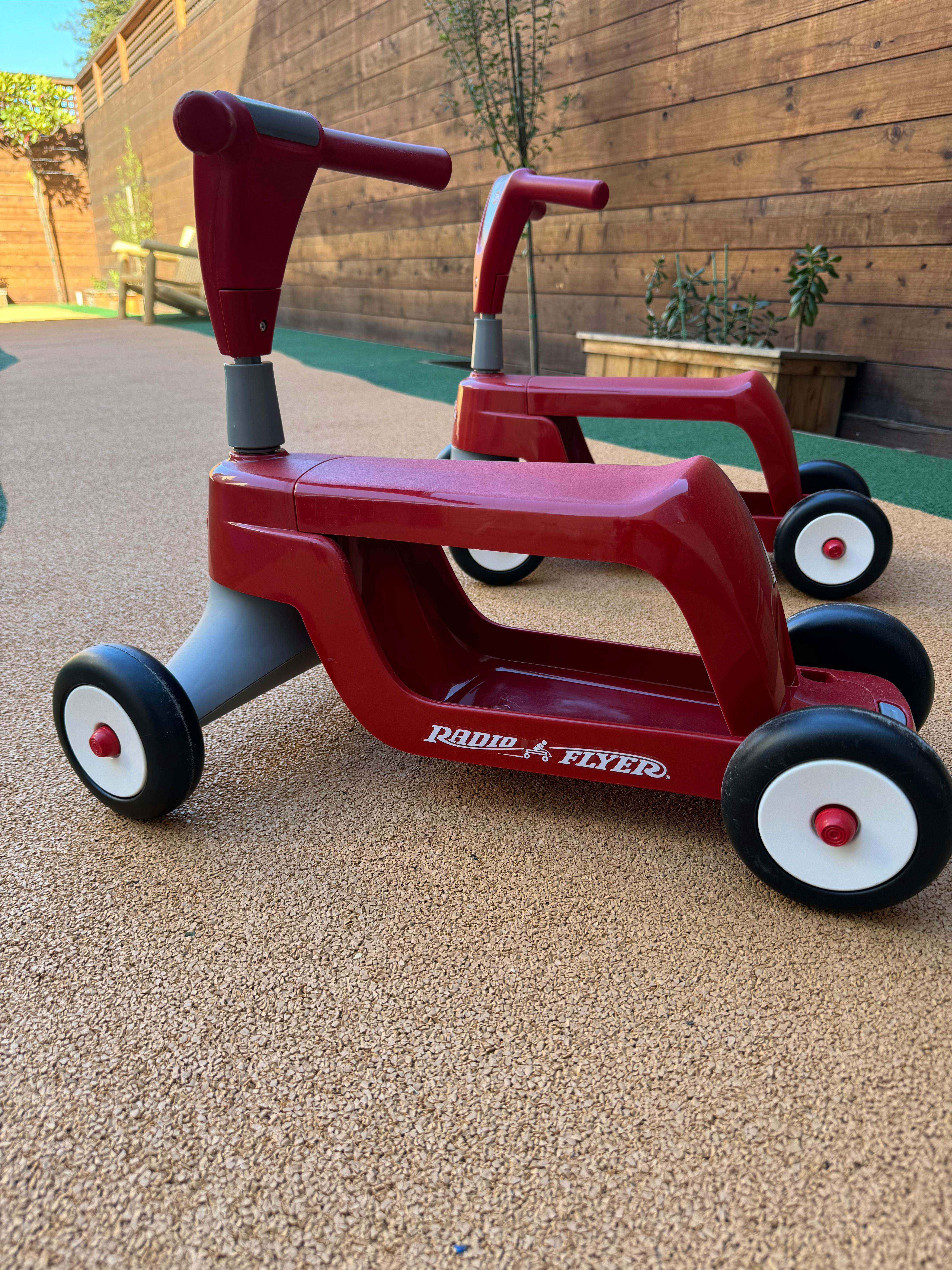 Two red Radio Flyer ride-on toys on a textured ground