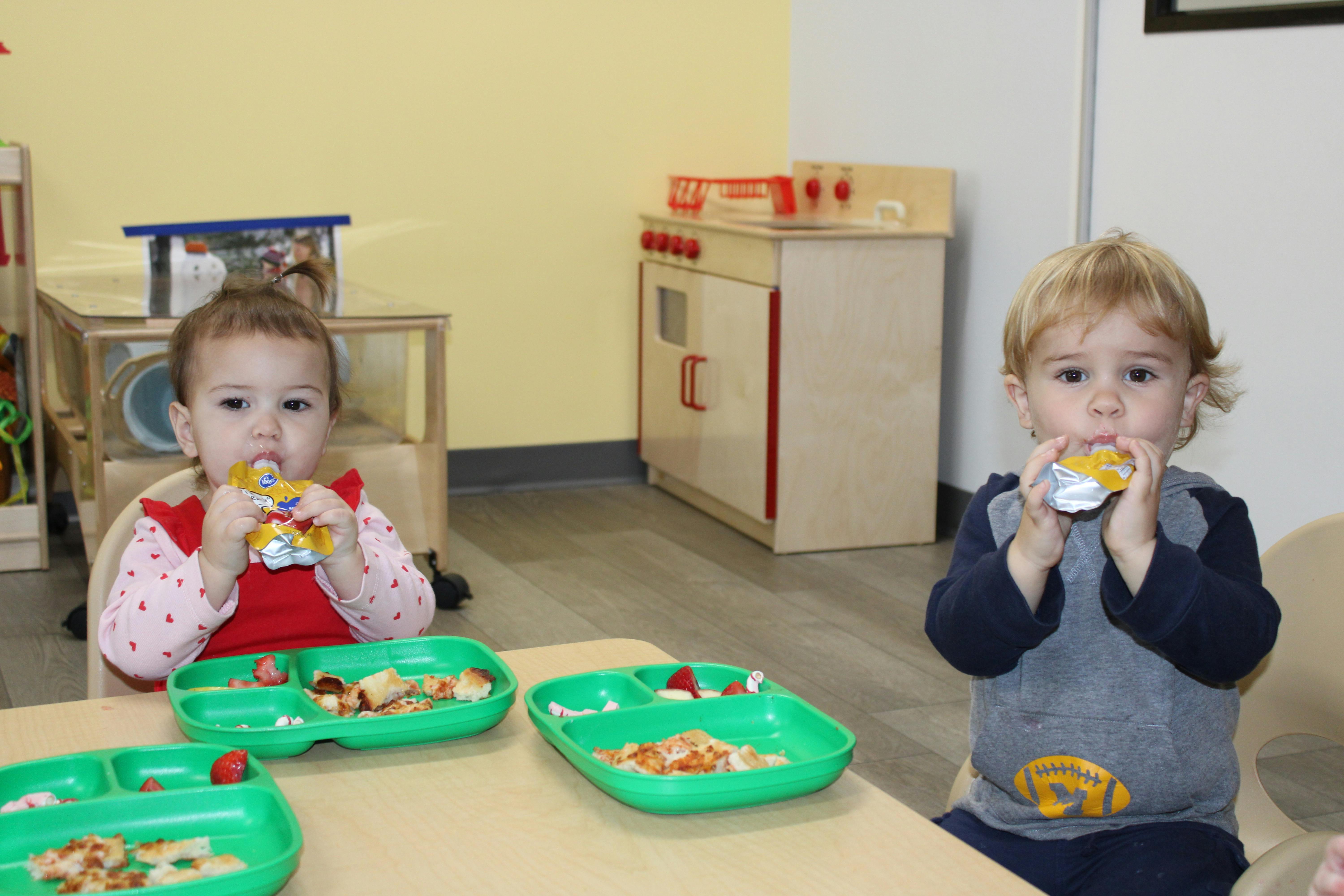 Two children eating from pouches and plates at a table
